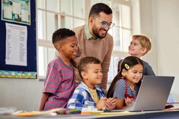 Happy smiling multiethnic children studying with teacher and computer